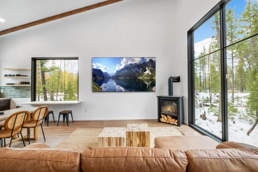 Bright living room with floor-to-ceiling windows showcasing nature and mountain scenery.