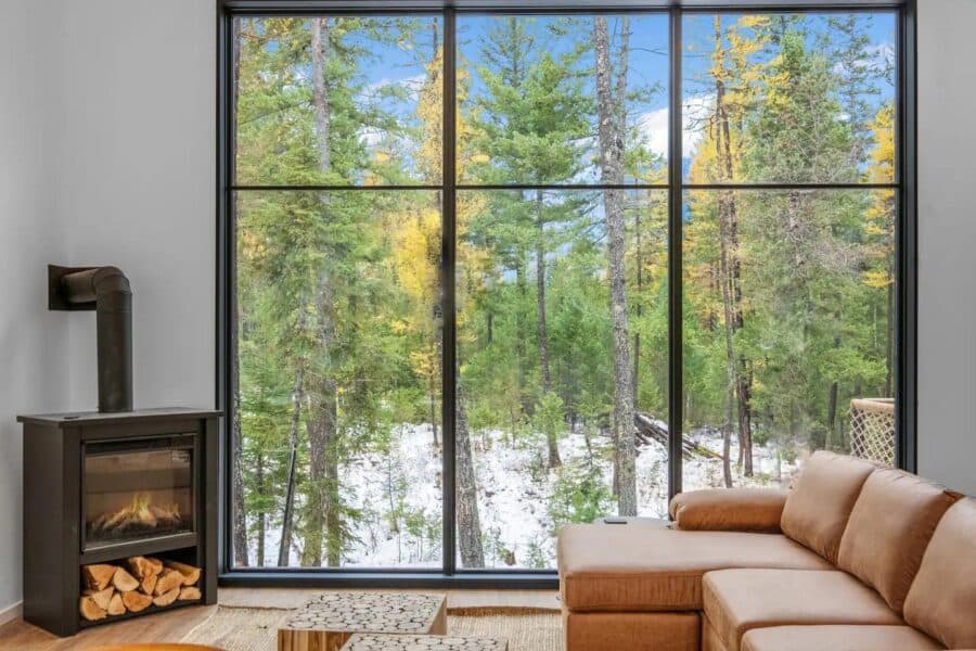 Bright interior of off-grid cabin with expansive window overlooking snowy forest landscape.