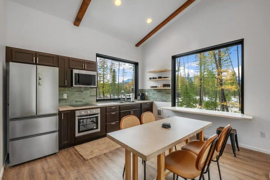 Compact off-grid cabin kitchen with modern appliances and large windows overlooking nature.