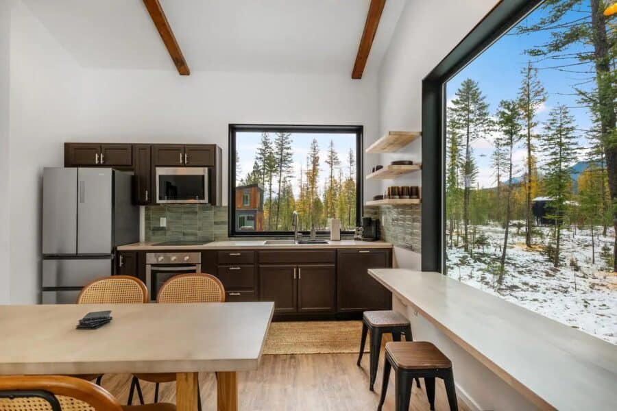 Modern off-grid cabin kitchen with large windows overlooking snowy landscape and forest.