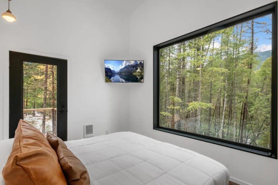 Interior of tiny cabin with large window overlooking lush forest landscape.