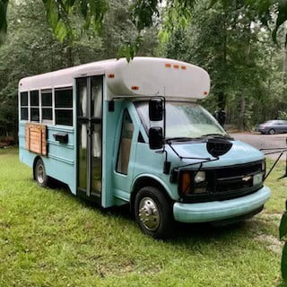 Pale blue French farmhouse style skoolie bus conversion parked on grass