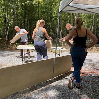 Workshop attendees working on a framed wall section outdoors at an off-grid camp in Georgia