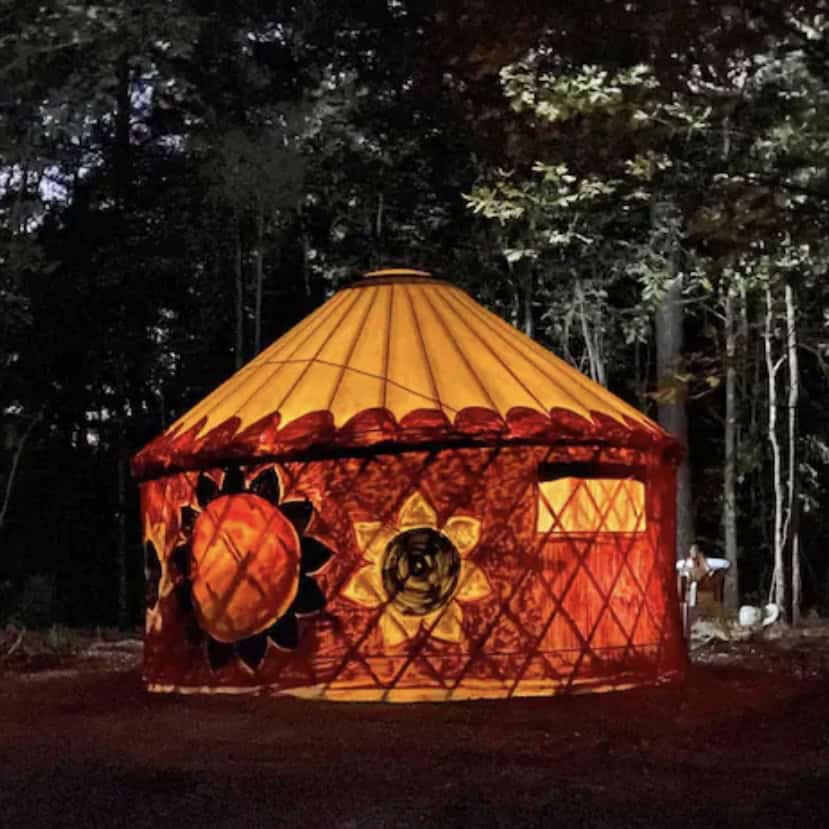Illuminated painted yurt at night in the woods at Beloved Cabin Homestead