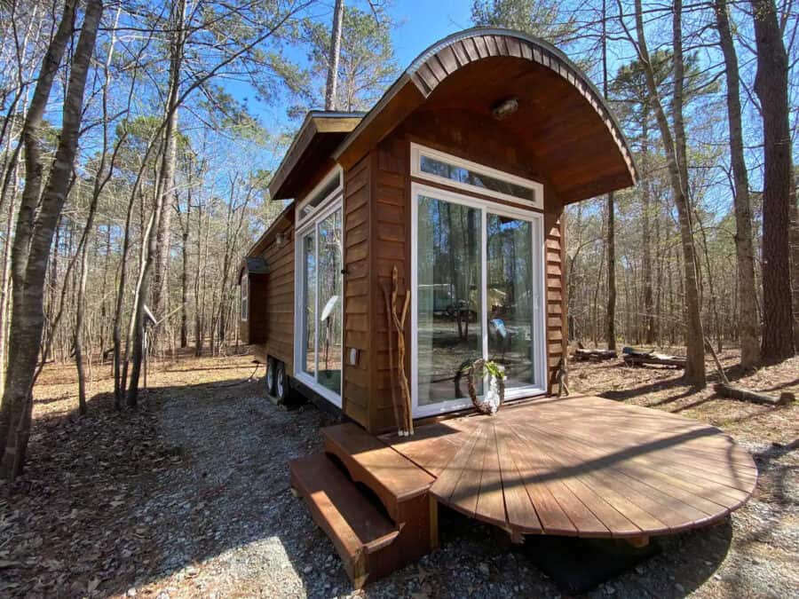 Off-grid tiny workshop with curved roof and large glass doors in wooded setting.