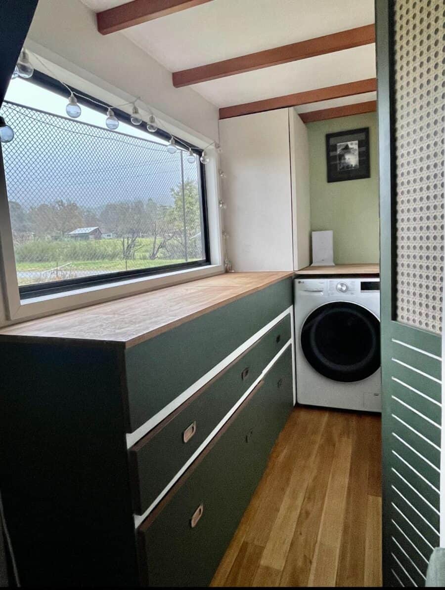 Efficient tiny house laundry space featuring green cabinetry and a front-loading washing machine.