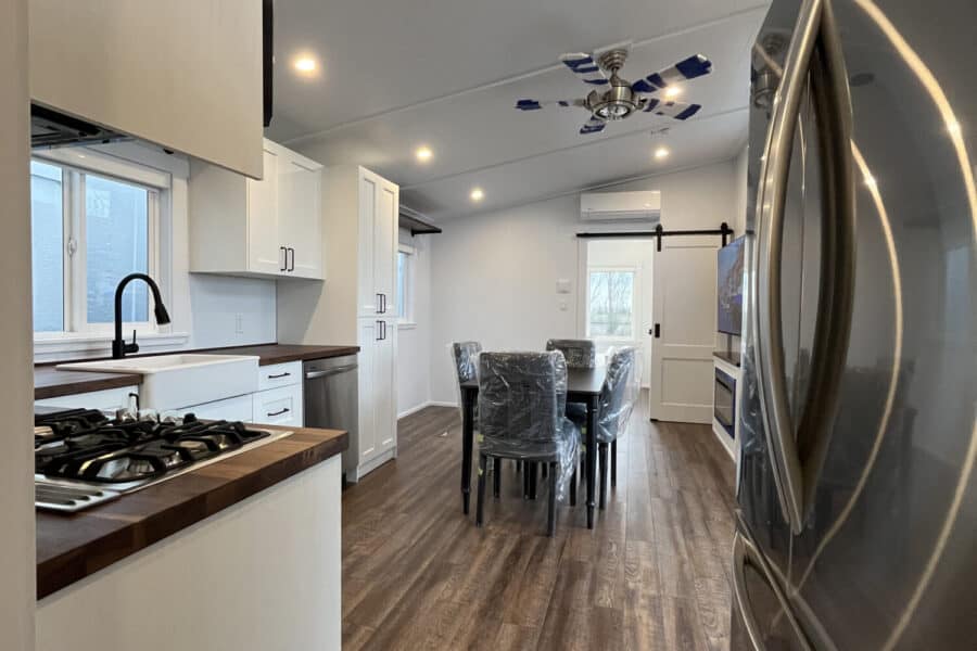 Modern tiny house kitchen with sleek white cabinets and wooden countertops, featuring a dining space.