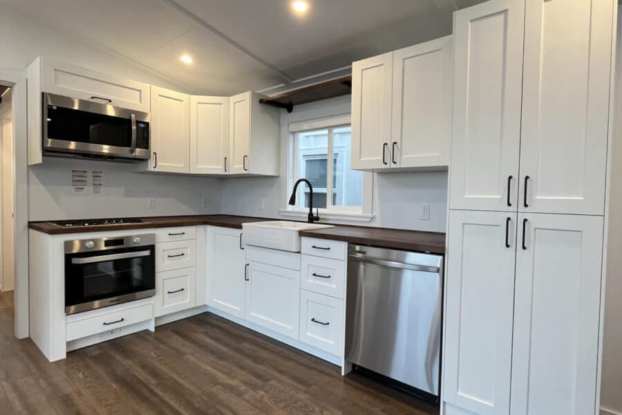 Modern tiny house kitchen with white cabinets and stainless steel appliances.