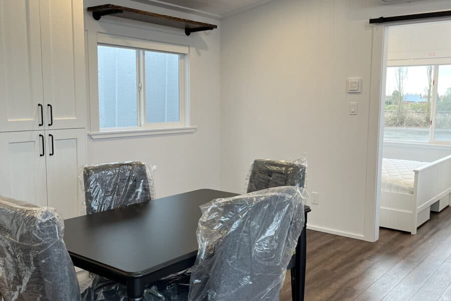 Compact tiny house dining space with a black table and four chairs covered in plastic.