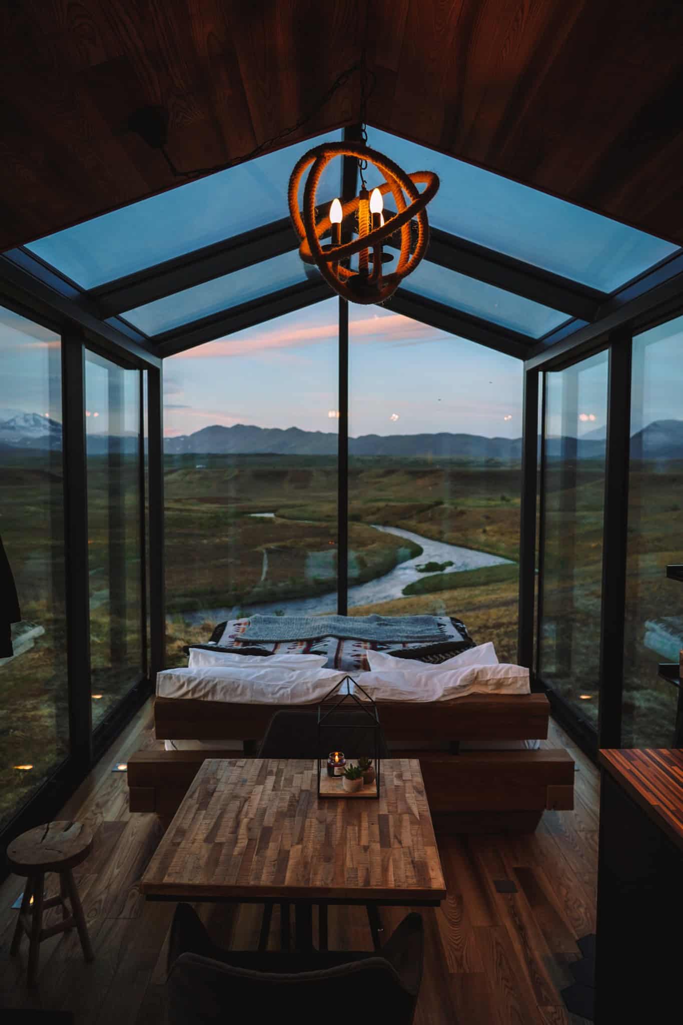 Interior of a Panorama Glass Lodge at dusk with bed, dining table, and river view