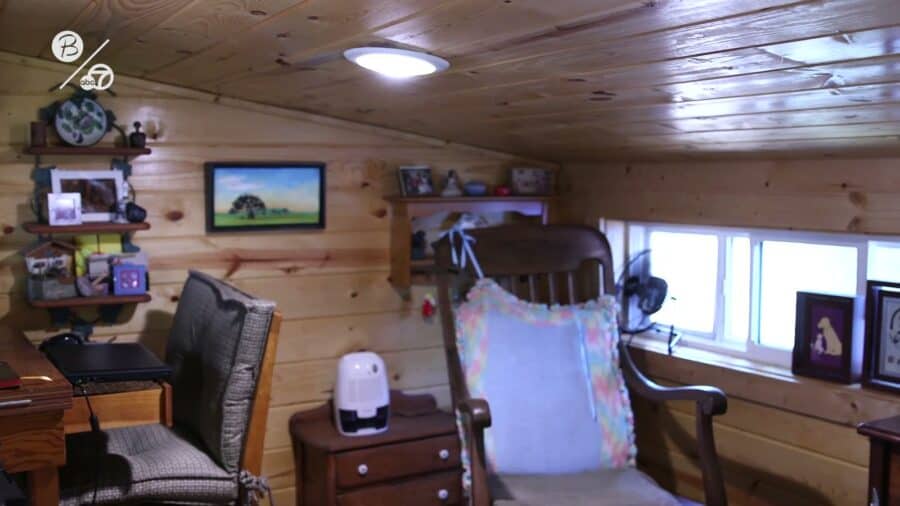 Pine-paneled living room with a rocking chair and desk inside Corrine Corley's 200 square foot tiny house