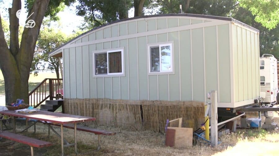 Sage green board-and-batten tiny house on wheels with a picnic table on G Row at Park Delta Bay