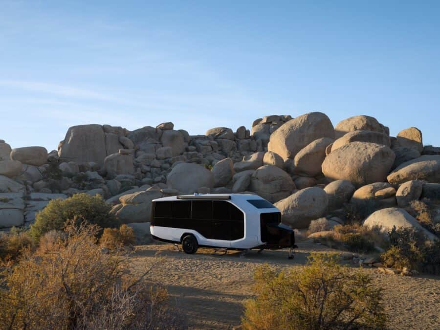 Modern tiny house trailer parked in rocky desert terrain under clear blue sky.