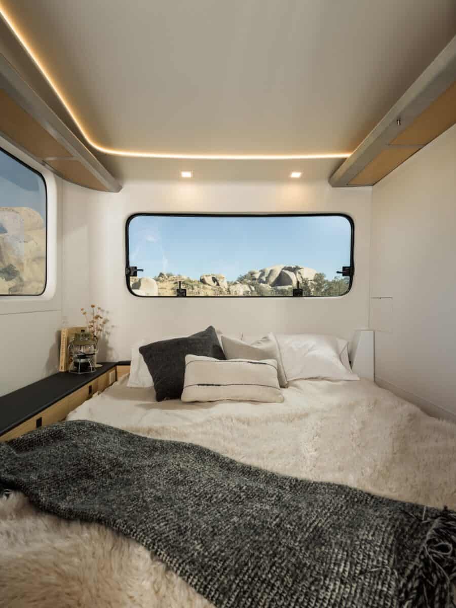 Compact tiny house bedroom with large windows and scenic outdoor views.