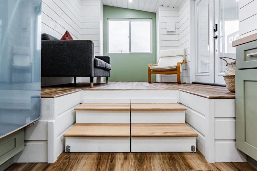 Cozy interior of a pine needle tiny home with stairs, sofa, and bright window.