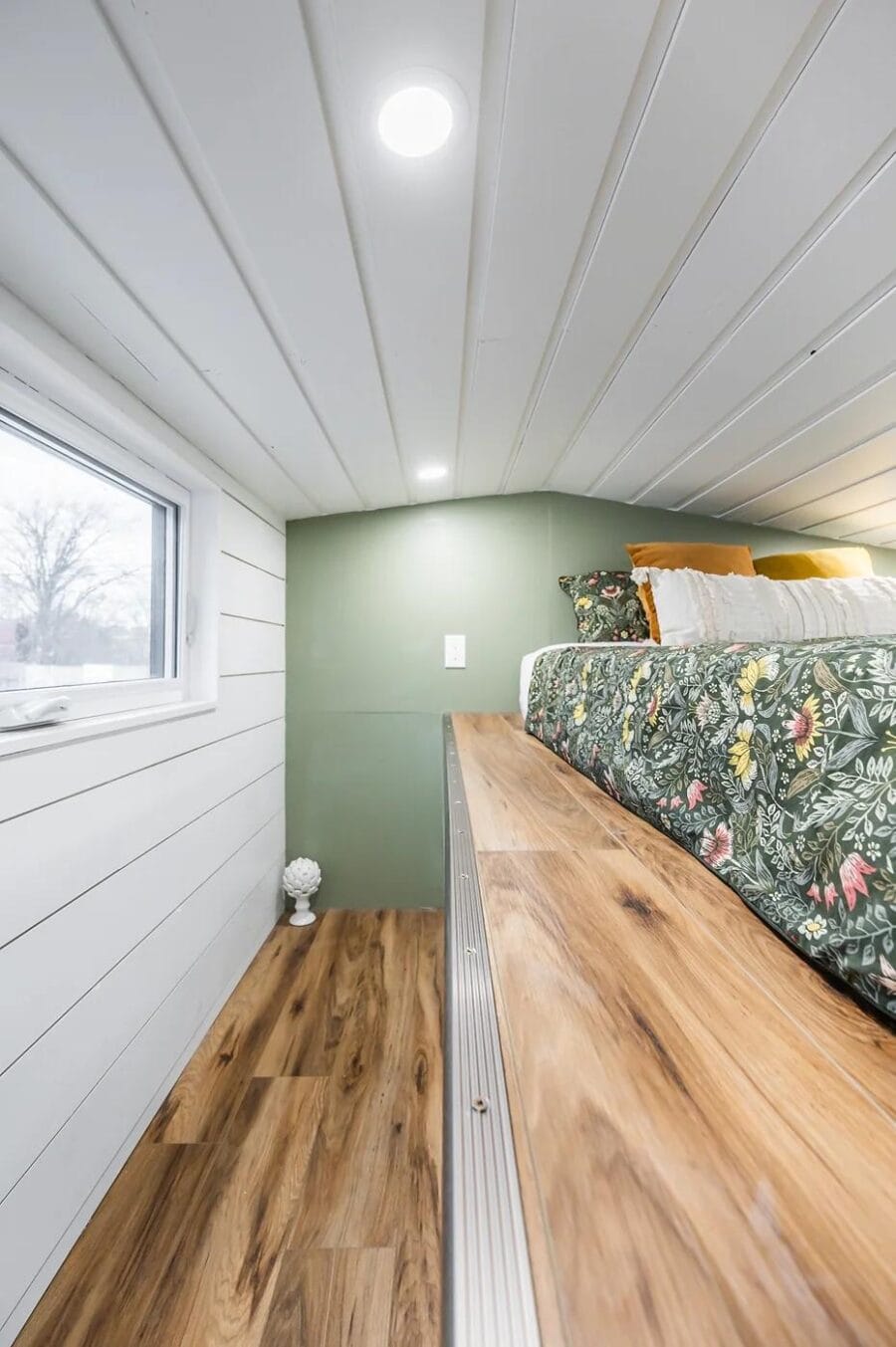 Cozy tiny house bedroom with green accent wall and wooden platform bed.