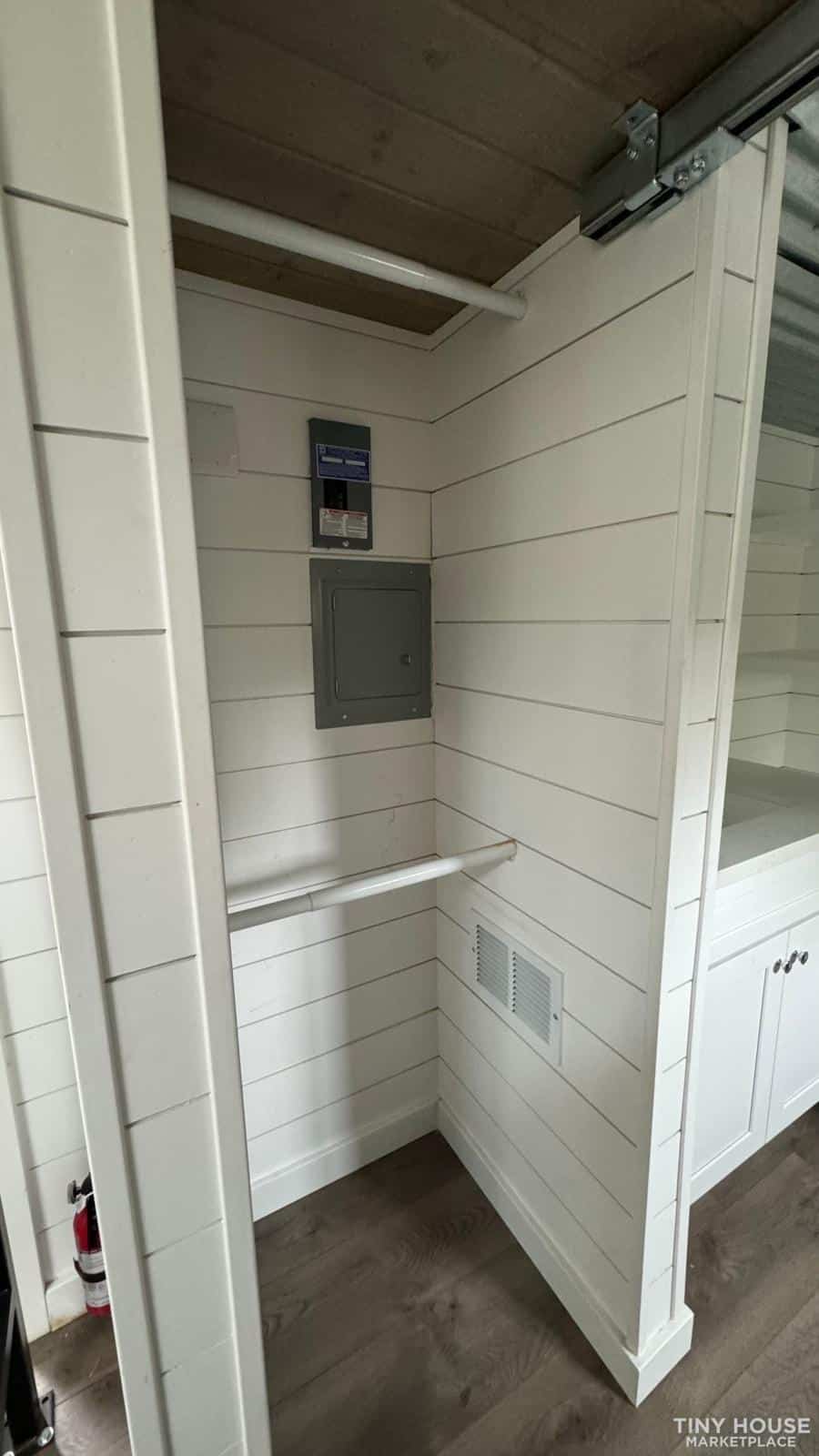 Interior view of a sage green tiny house with white panel walls and storage features.