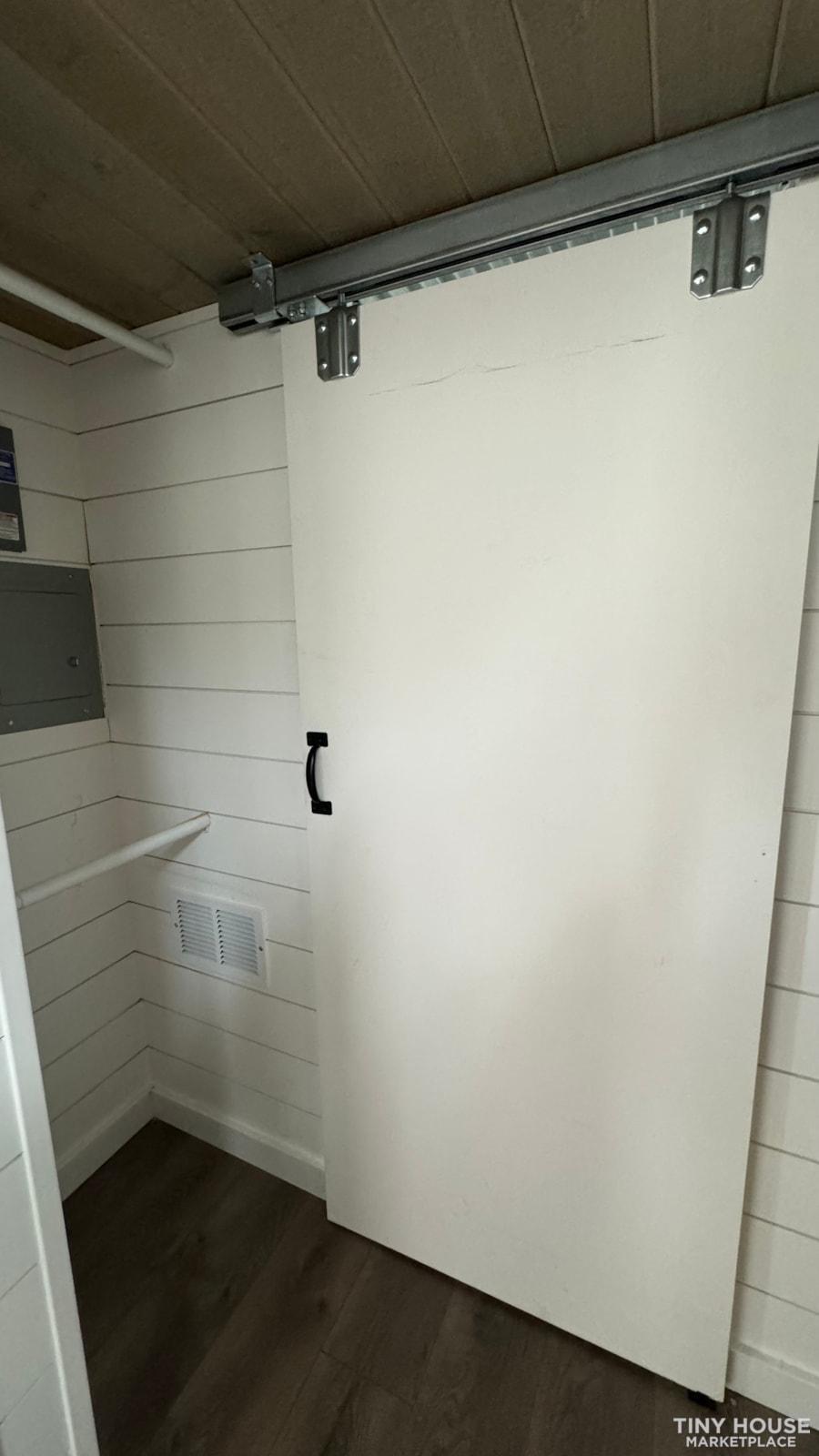 Sliding barn door in a tiny house interior with white shiplap walls.