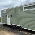 Sage green tiny house on wheels with modern design and small windows.