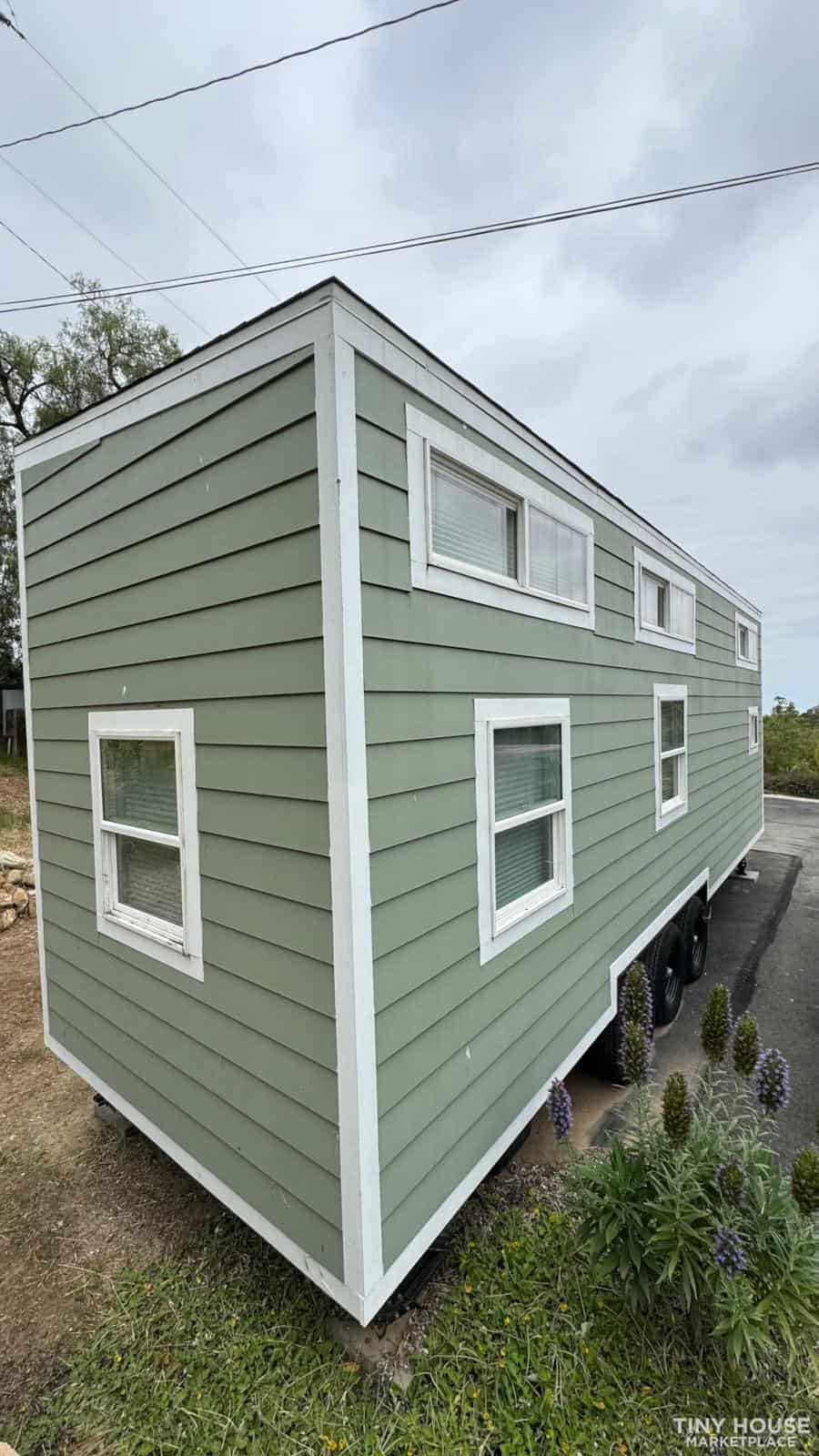 Sage green tiny house with multiple windows on a trailer, modern small space living.