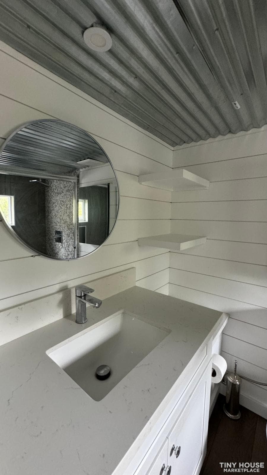 Bright sage green tiny house bathroom with modern sink and round mirror.