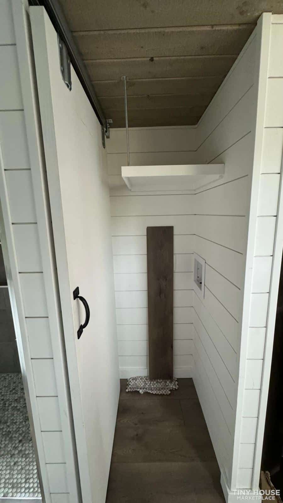 Compact tiny house storage nook with shelves and wall paneling.