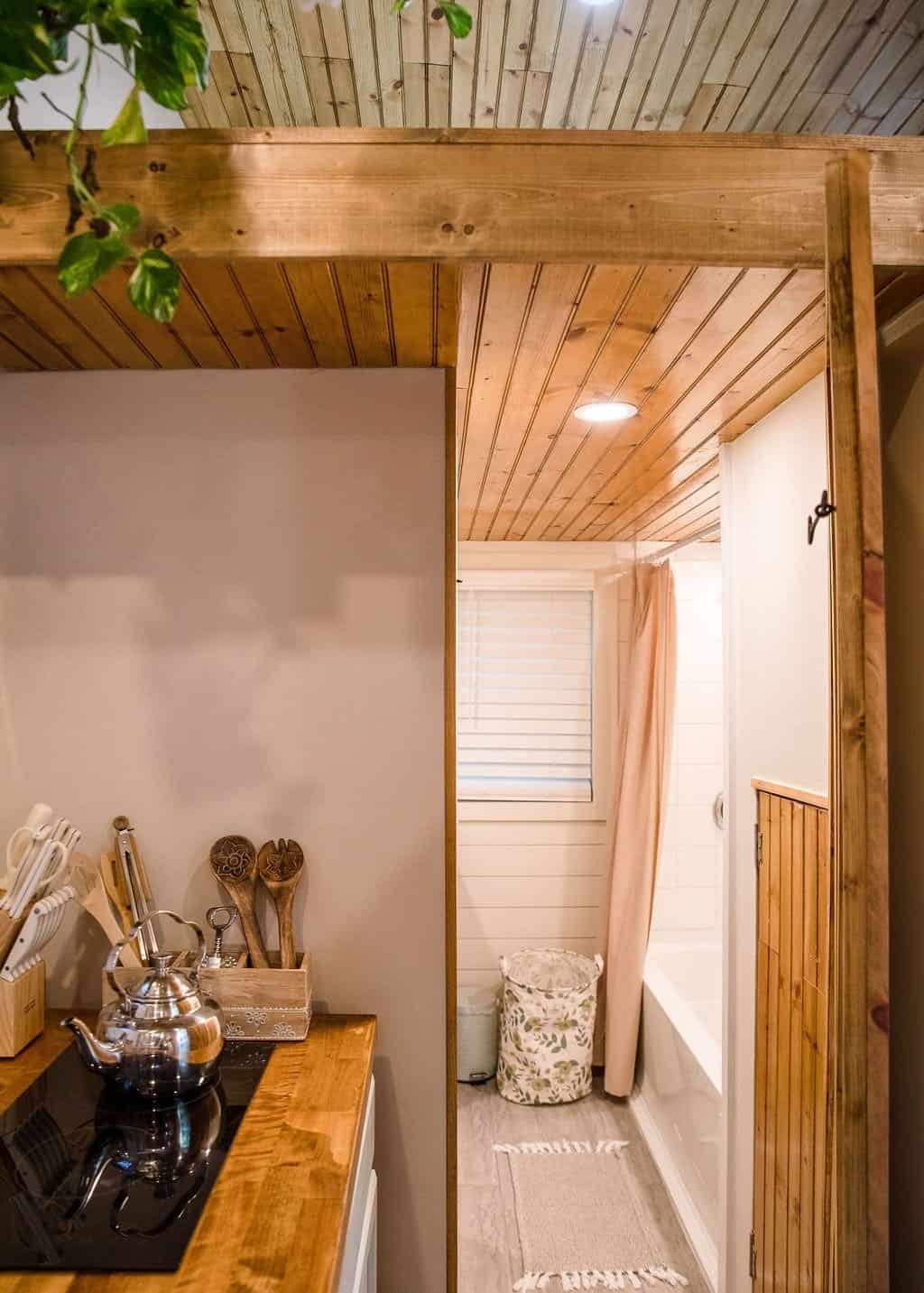 Prana tiny house kitchen cooktop beside the full bathroom, which has a full-size tub with a tile surround and a window