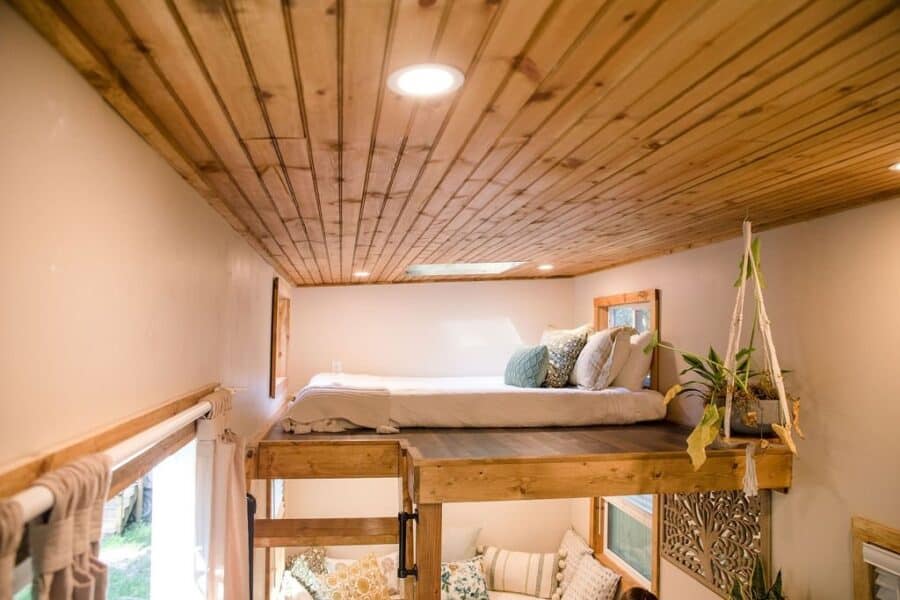 Sleeping loft in the Prana tiny house with a skylight and pine ceiling, overlooking the cushioned living nook below