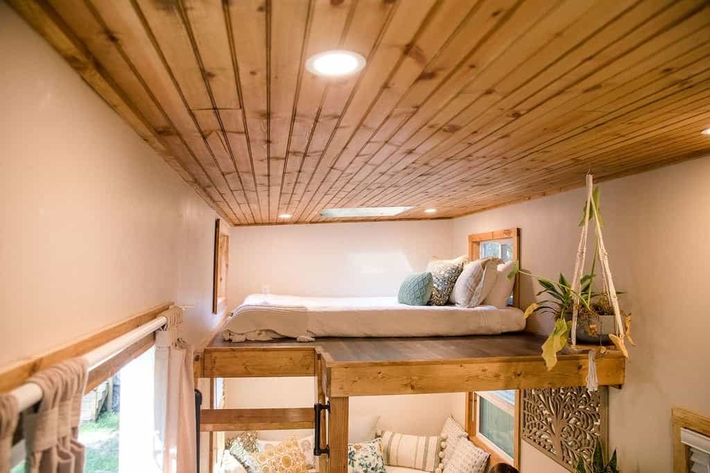 Sleeping loft in the Prana tiny house with a skylight and pine ceiling, overlooking the cushioned living nook below