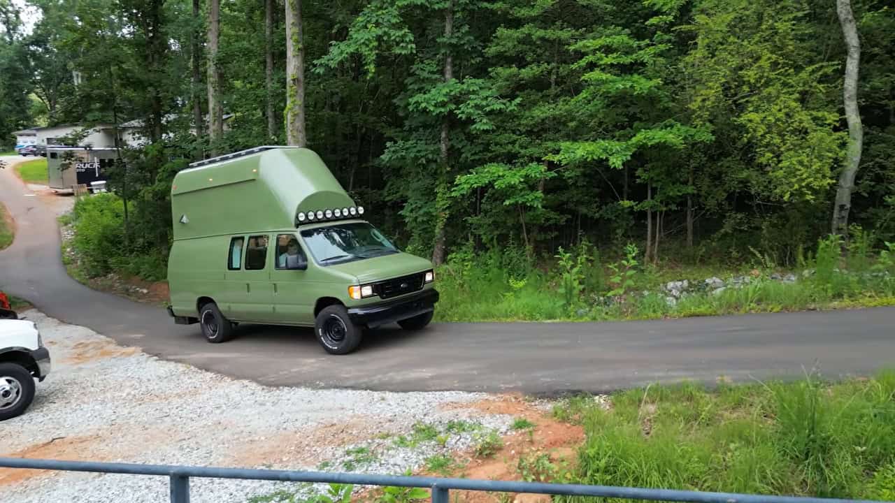 The finished two-story van driving down a wooded road