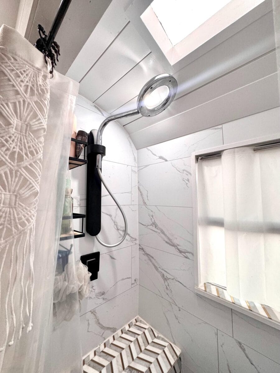 Shower in a compact tiny house bathroom with modern fixtures and marble accents.