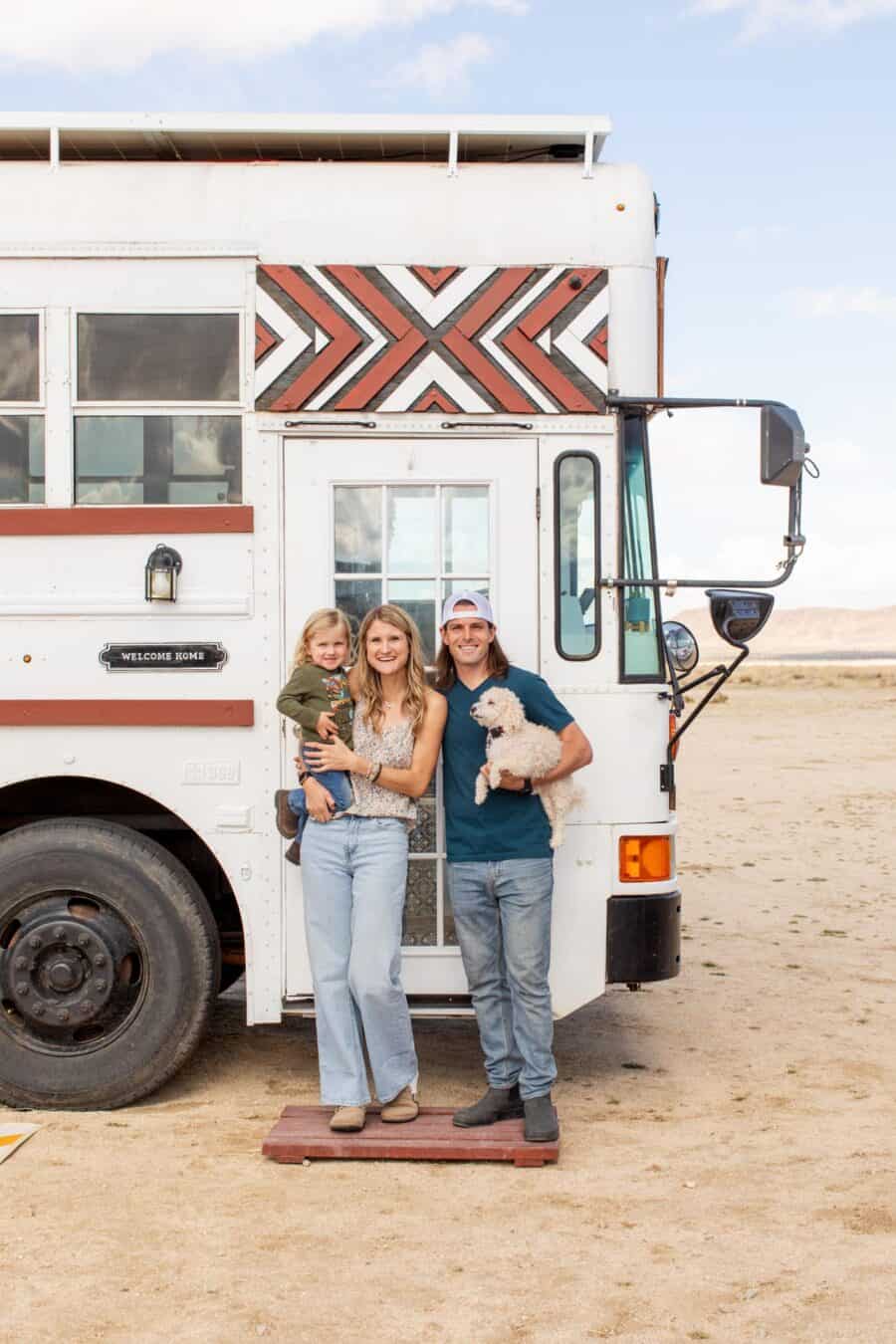 Family of three with dog in front of a colorful skoolie tiny house on a desert landscape.