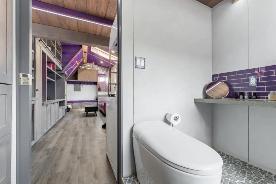 Modern tiny house bathroom with sleek toilet and stylish purple tile backsplash.