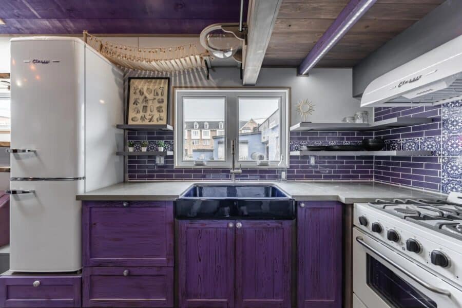 Compact tiny house kitchen with purple cabinetry and modern appliances.