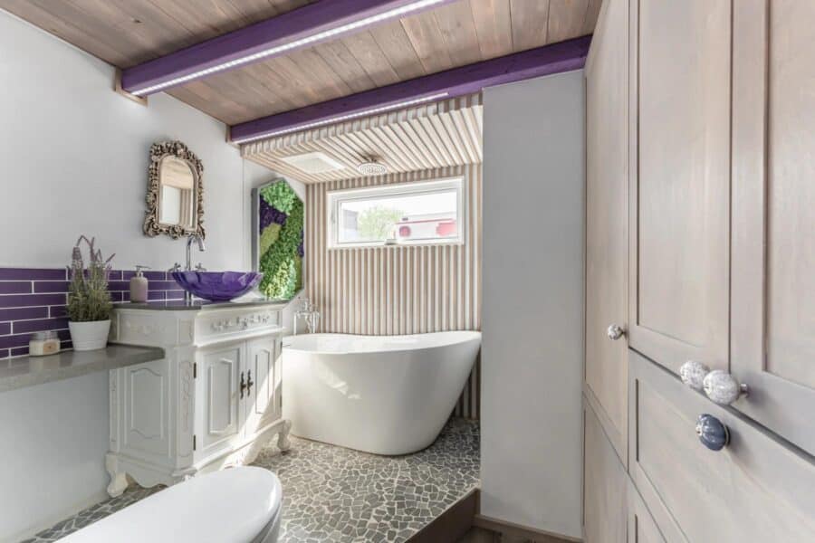 Charming tiny house bathroom featuring a modern bathtub, purple decor, and natural light.