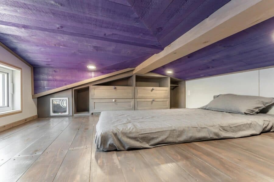 Attic bedroom with purple and natural wood accents in Purple Heart Manor by Acorn Tiny Homes.