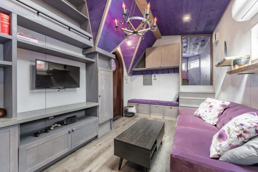 Bright and cozy tiny home living room with purple accents and unique ceiling design.
