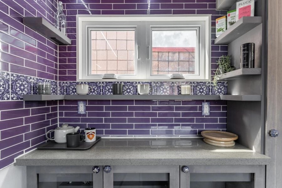 Compact tiny house kitchen with purple tile backsplash and modern shelving.