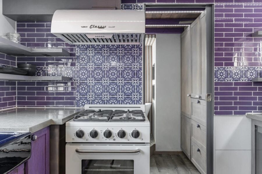 Compact tiny house kitchen featuring purple tile backsplash and modern appliances.