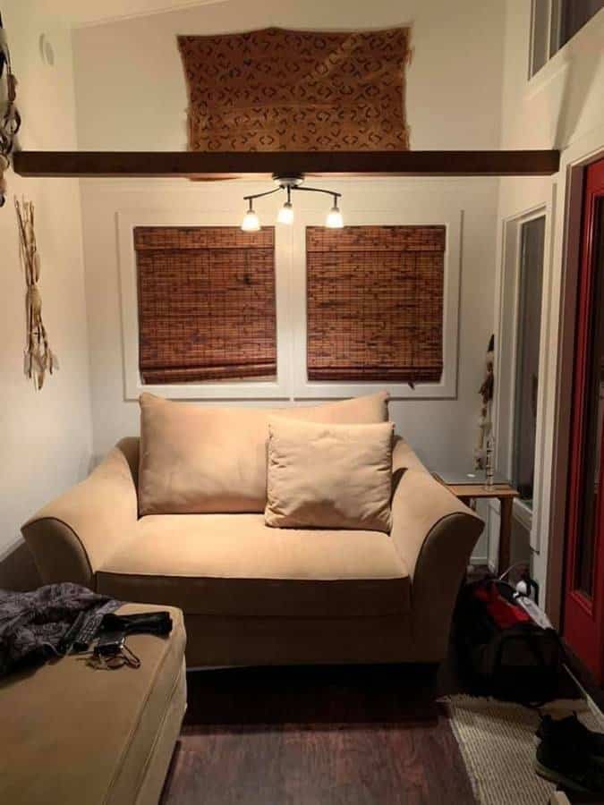 Compact tiny house interior with a beige sofa and woven window shades.