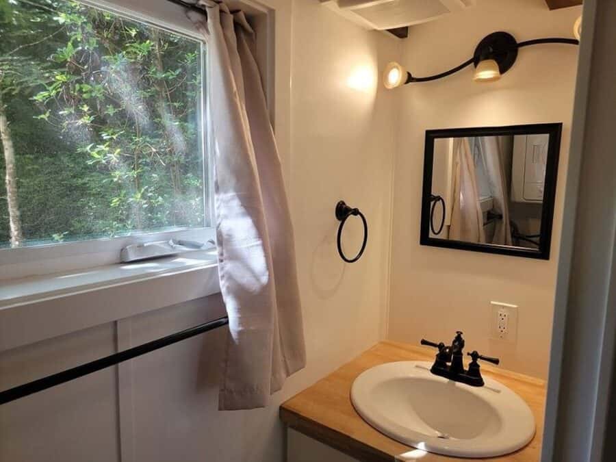 Bright tiny house bathroom with a large window and simple fixtures.