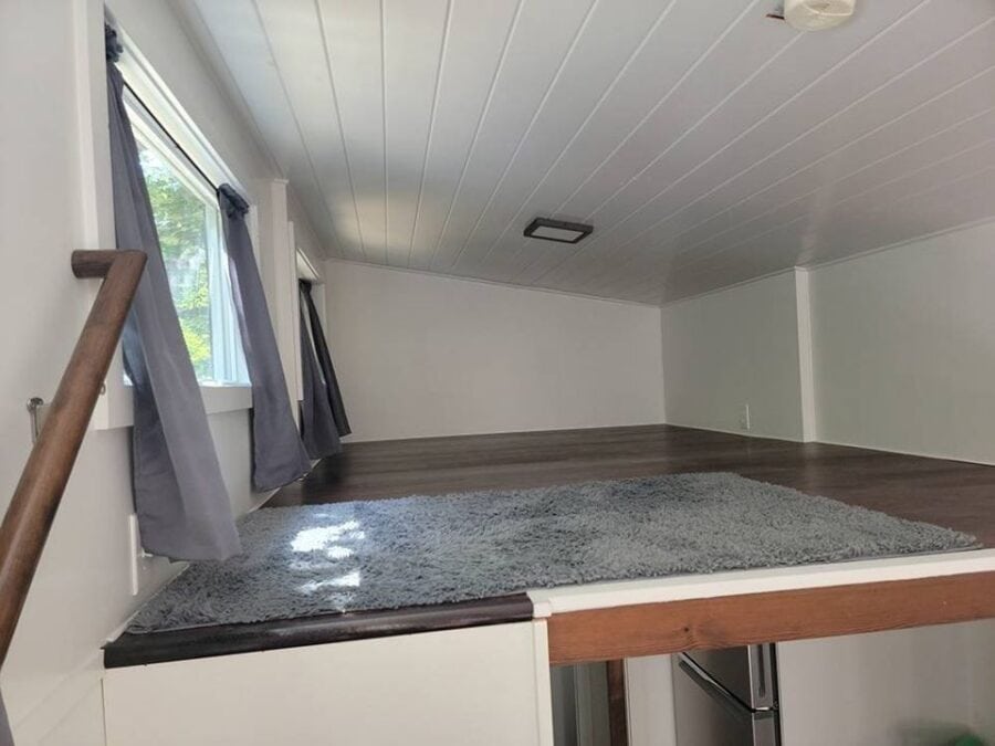 Cozy tiny house interior with sloped ceiling, large window, and hardwood floor.