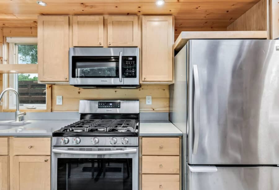 Compact tiny house kitchen featuring stainless steel fridge, microwave, and stove for efficient smal.