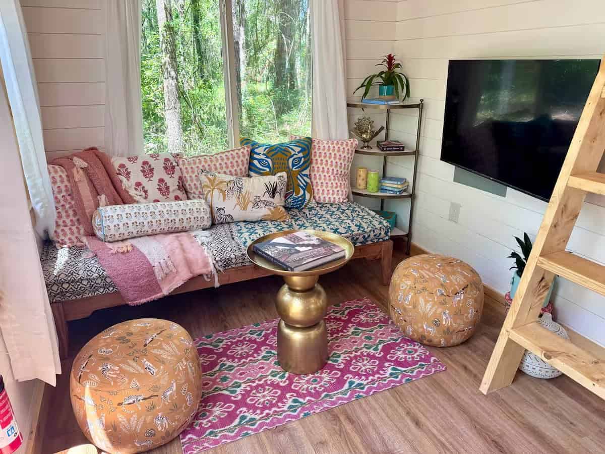 Boho living nook in the Rasa tiny home with patterned cushions, a brass table, poufs, and a swivel smart TV