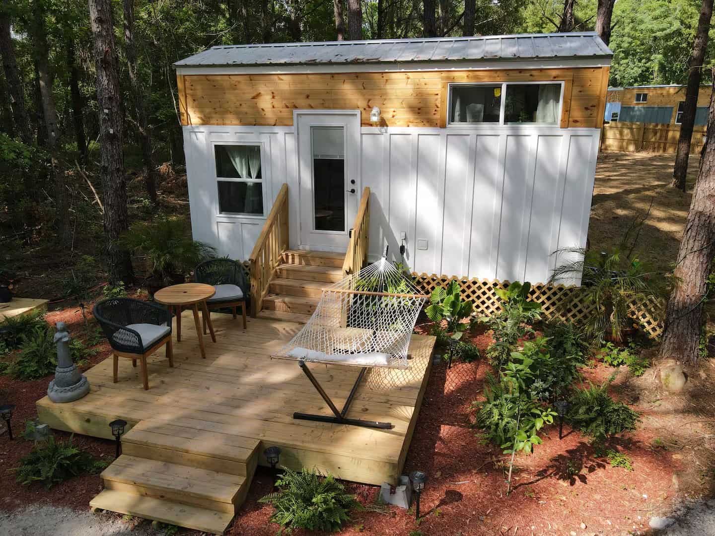 Elevated view of the Rasa tiny home's wood deck with a hammock, rope chairs, and lattice skirt