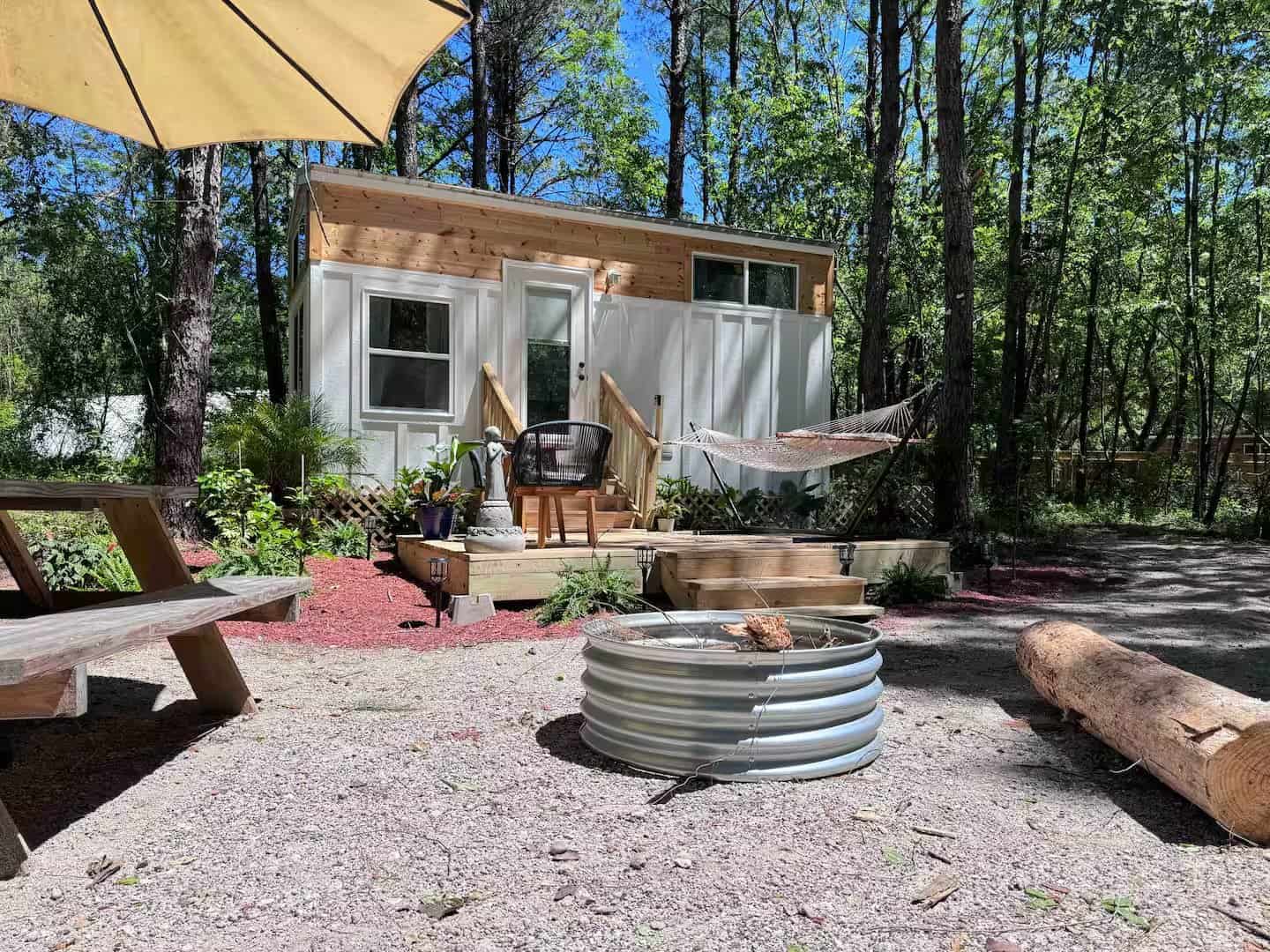 Rasa tiny home with an umbrella-shaded picnic table, fire pit, and hammock in the woods