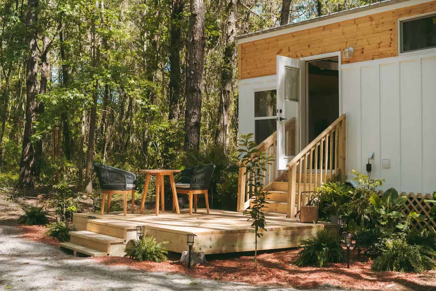 Front deck of the Rasa tiny home with rope chairs, a bistro table, and lush plantings