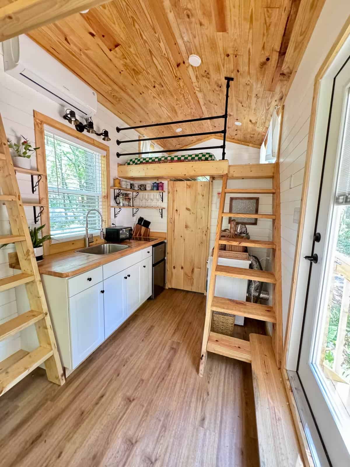 Galley kitchen in the Rasa tiny home with butcher block counters, loft ladders, and a glass door to the woods