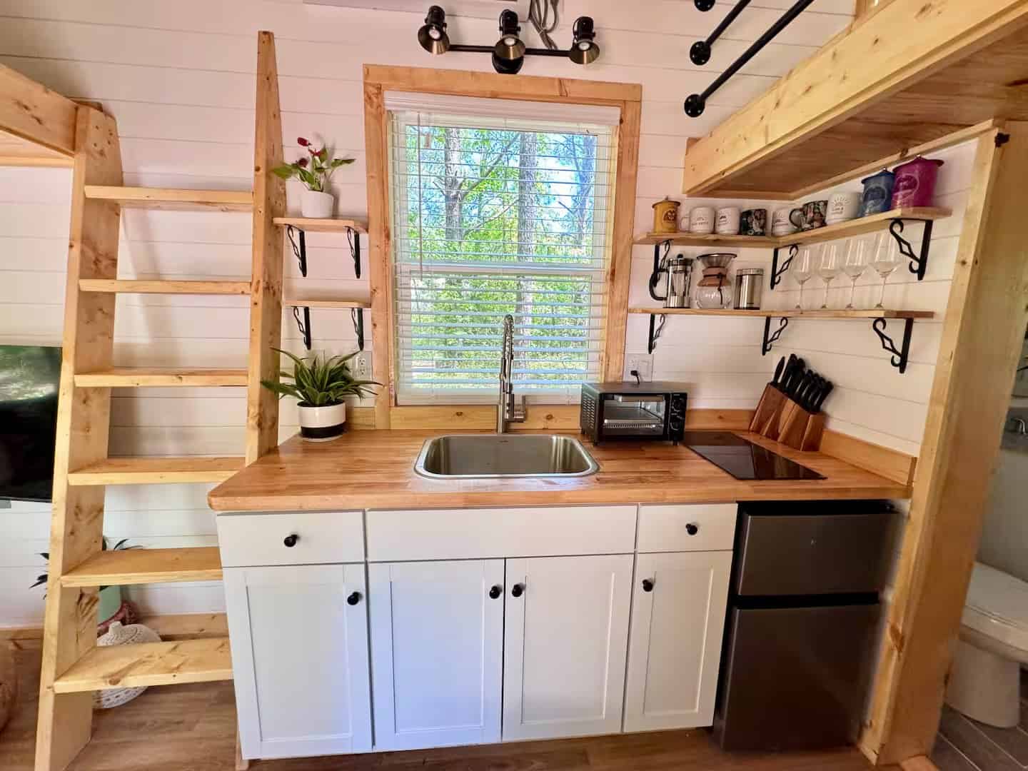 Rasa tiny home kitchenette with a stainless sink, electric cooktop, toaster oven, mini-fridge, and open shelving