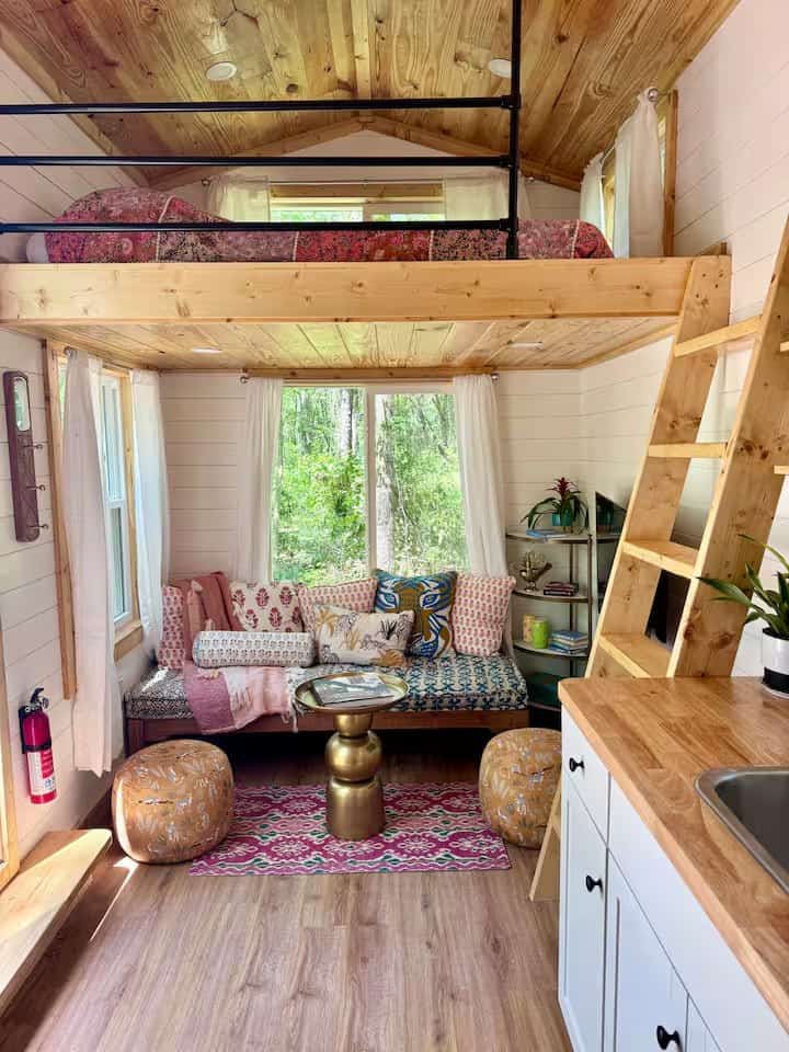 Rasa tiny home living area with a cushioned daybed under big windows and a sleeping loft above